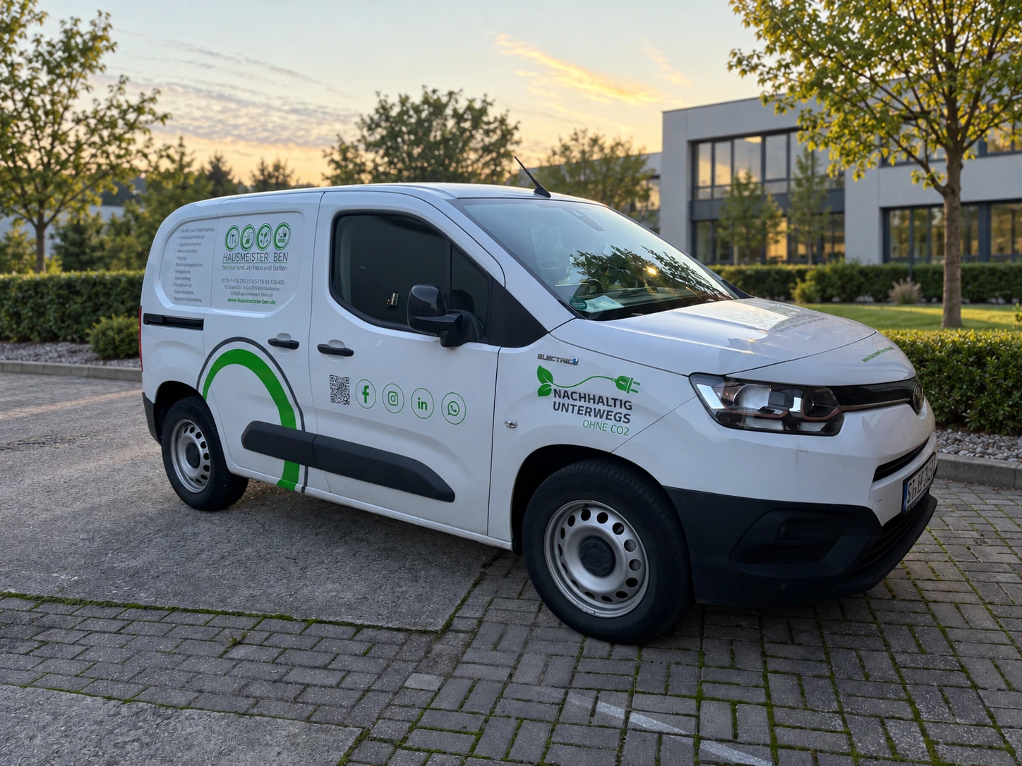 Weißes HMB-Elektrofahrzeug mit grüner Firmenbeschriftung vor einer gepflegten Gewerbeimmobilie
